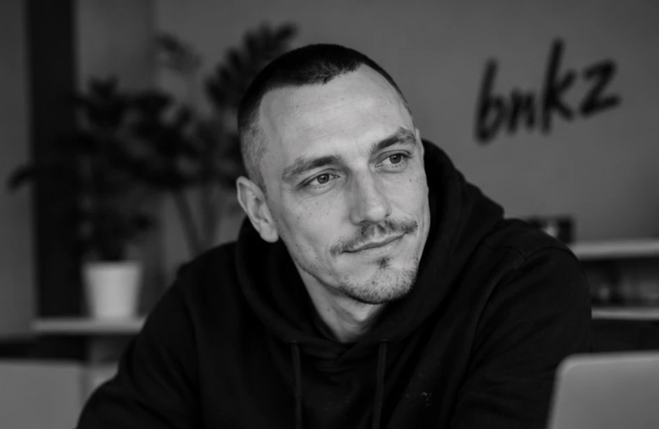 Tassilo Wolfin an seinem Schreibtisch, im Hintergrund steht handschriftlich bnkz an der Wand.